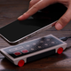 A hand placing a smartphone on the 8BitDo N30 Wireless Charger for Mobile sitting on a wooden table.